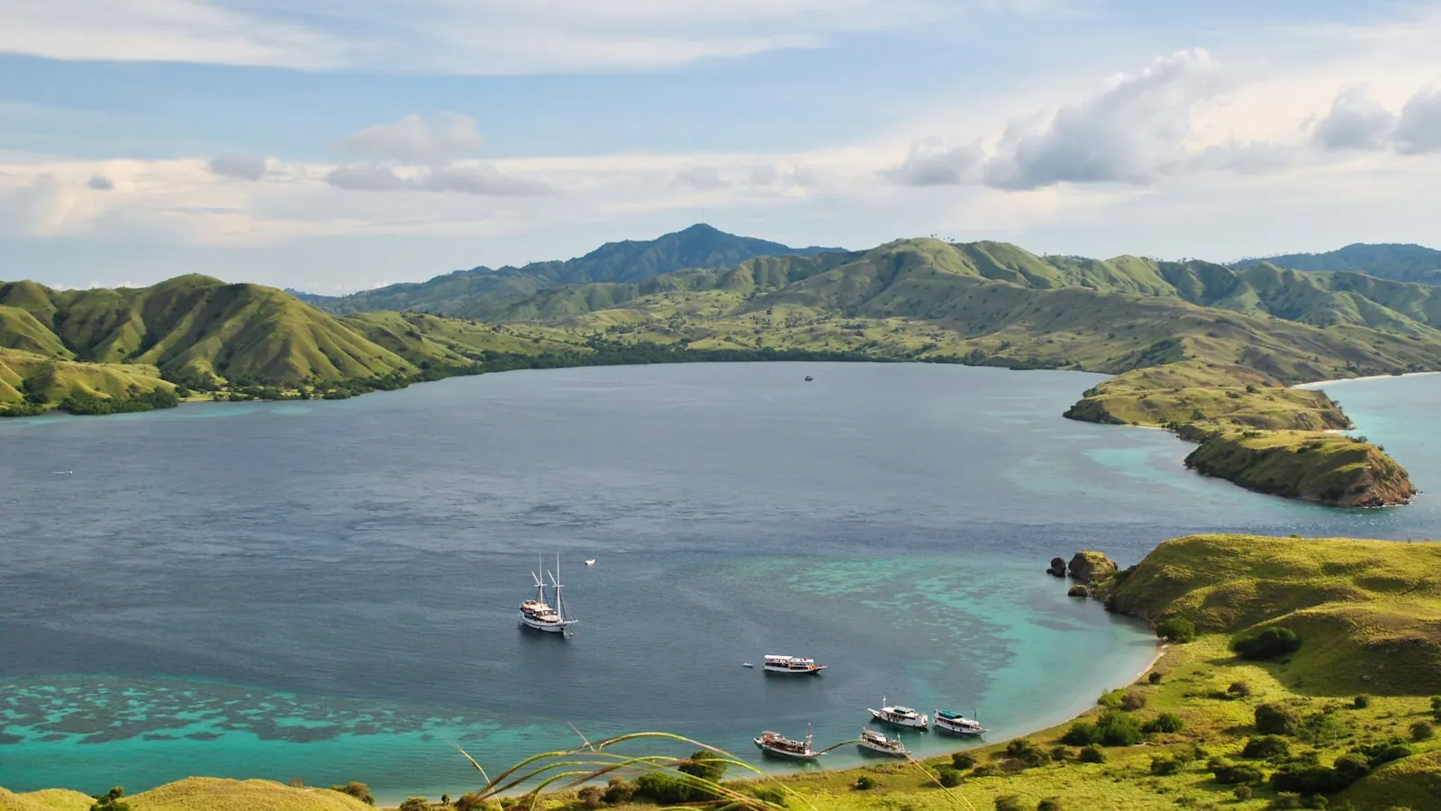 Luxury Phinisi yacht sailing through vibrant turquoise waters past dramatic green islands in Komodo National Park, Indonesia.